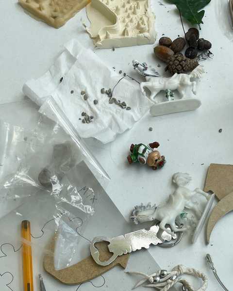 Photo of the working process on silicone tiles that are part of the installation "Love story of a ghost" by Julia Rosenstock. Visible are test objects including a plastic horse, acorns, a pen, MDF wooden shapes resembling arrows and a house, and a bottle opener.