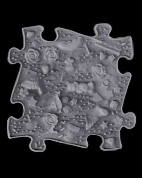 Scan of a gray silicone mat shaped like a puzzle. The mat features various forms arranged as if floating around—a teddy bear, a cross, an Eiffel Tower souvenir, roses, stars of various sizes, and hearts. In between the forms, the surface of the tile is covered with protrusions of different heights. This silicone puzzle mat is part of a larger mat floor installation in Julia Rosenstock’s work "Love story of a ghost".