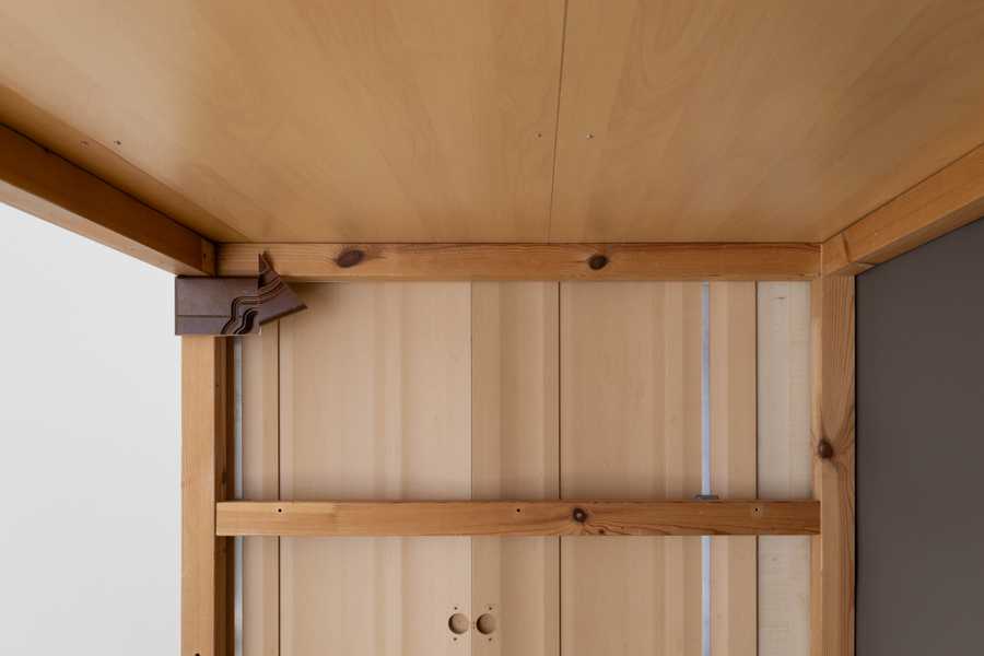  Installation view of Charms (2025) by Julia Rosenstock: a 30-minute video projected within a custom frame, accompanied by two-channel sound transmitted through resonant surfaces in the gallery. A bench sits in the space alongside wall-mounted reliefs made from plastic foil-coated MDF with walnut and oak veneer.