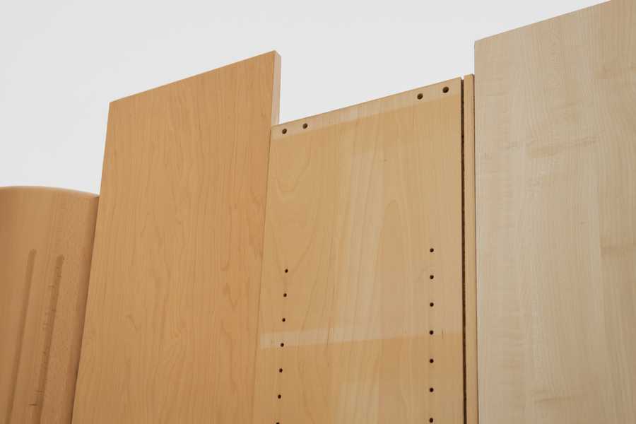  Installation view of Charms (2025) by Julia Rosenstock: a 30-minute video projected within a custom frame, accompanied by two-channel sound transmitted through resonant surfaces in the gallery. A bench sits in the space alongside wall-mounted reliefs made from plastic foil-coated MDF with walnut and oak veneer.